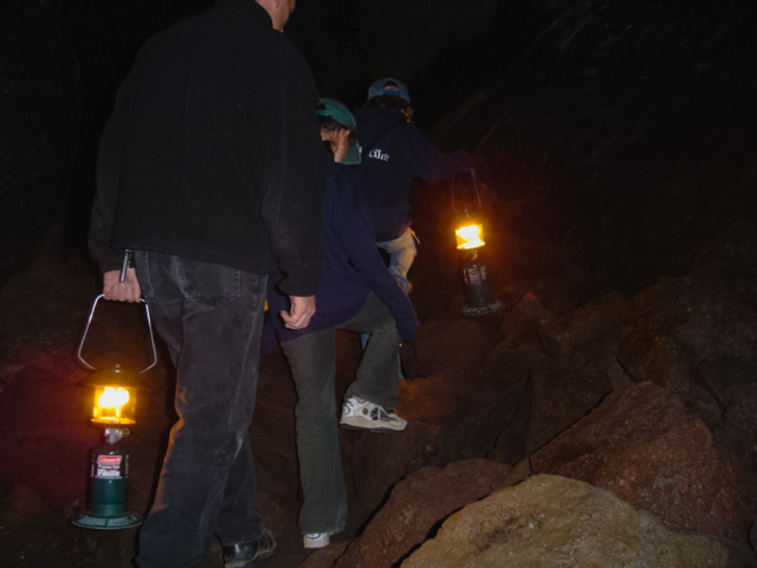 Girl standing in a large, very dark lava tube with flashlight in hand.